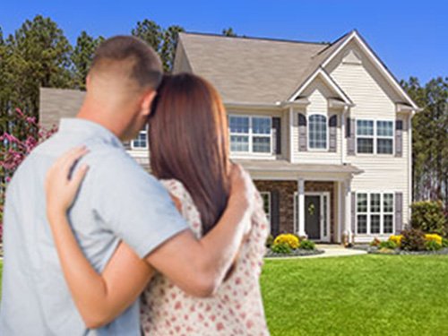 a young couple with their arms around each other are viewing a rental home front the front yard
