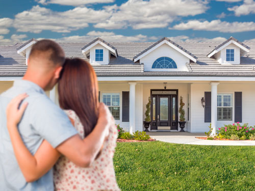 a young couple with their arms around each other viewing a rental home from the front yard